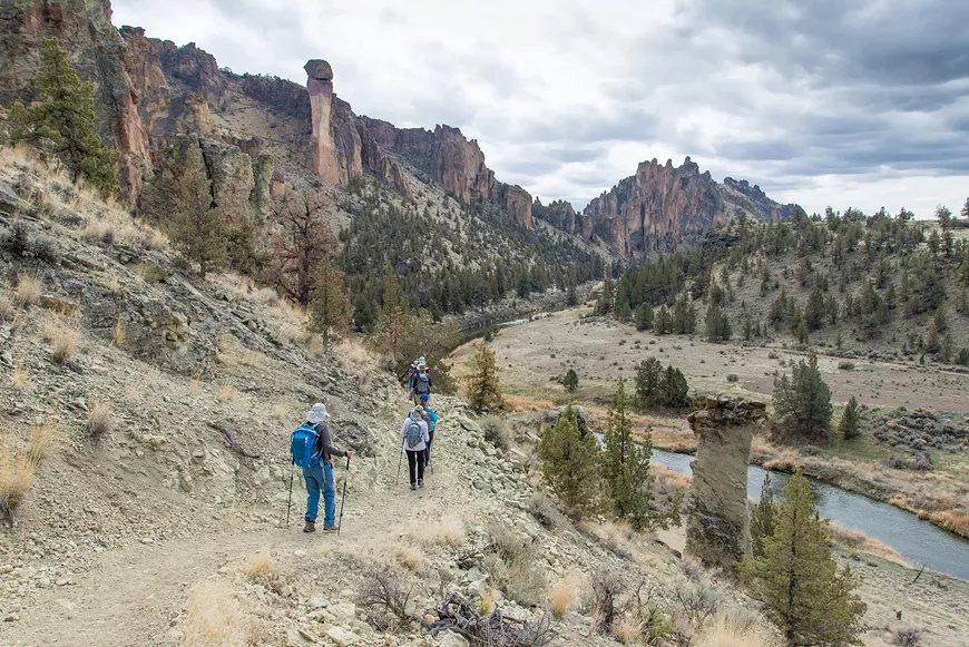 Hikers walk above the Crooked River with Monkey Face at Smith Rock in the background.