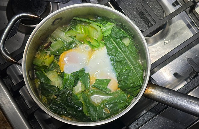 Ramen on the stove with greens and eggs at top